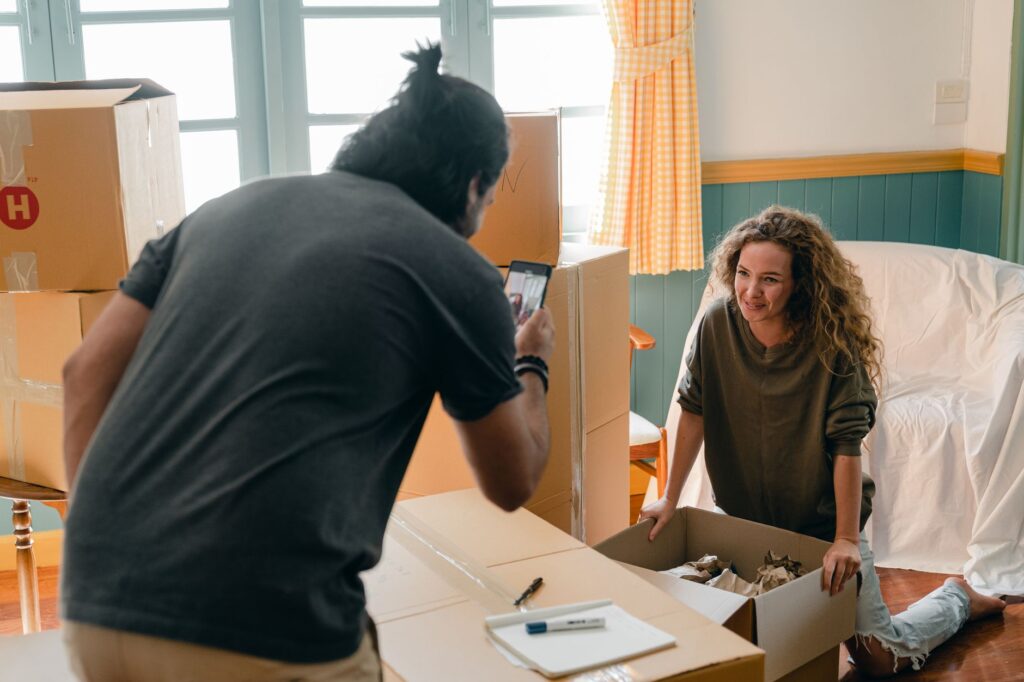 Person using a smartphone or tablet to photograph moving boxes and furniture in an apartment room for an AI-powered moving quote scan.