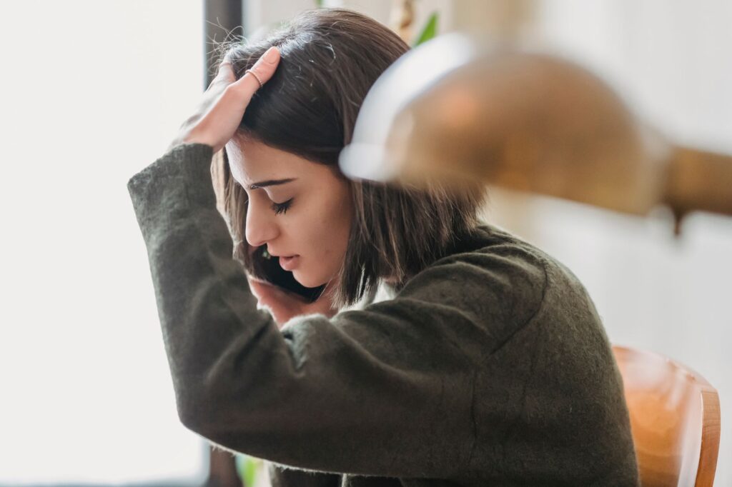 Frustrated young woman holding her head while waiting on hold during a phone call to get a moving quote.