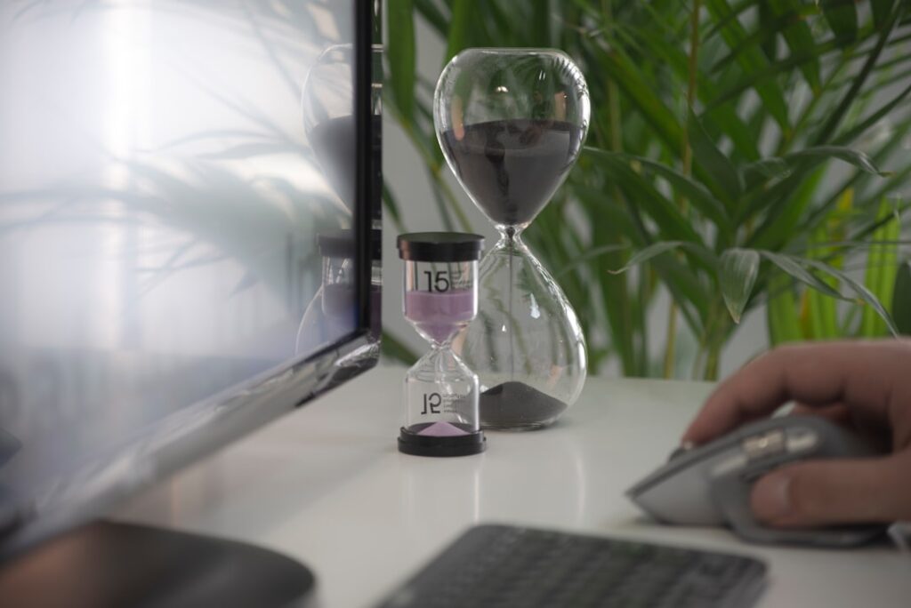 Hourglass on a desk next to a computer monitor, symbolizing time savings from AI tools