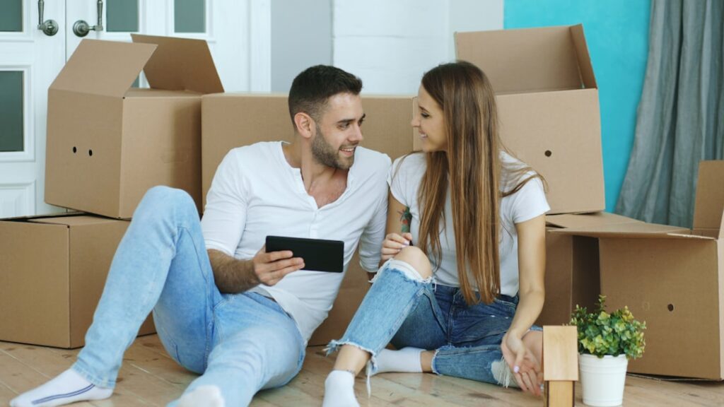 Young couple using a tablet surrounded by moving boxes in their new home, representing AI-powered moving quotes