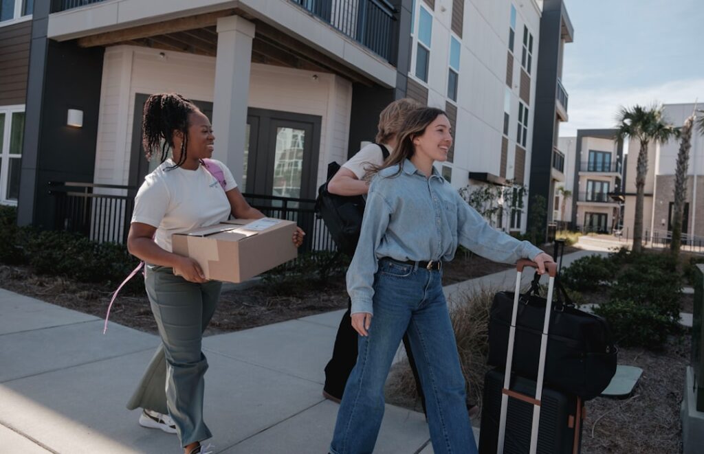 People carrying moving boxes and luggage outside an apartment building during a local move